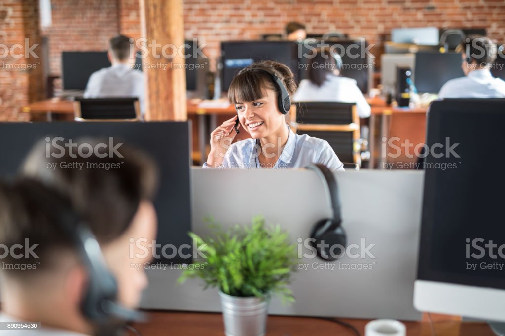 Call center worker accompanied by her team. Smiling customer support operator at work. Young employee working with a headset.